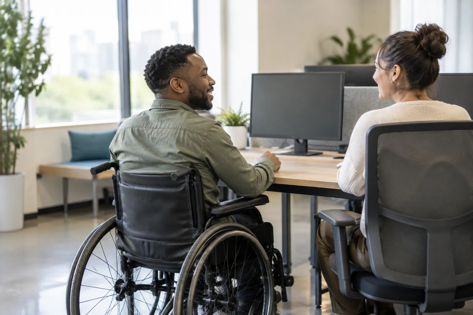 Adult using a wheelchair working with a coworker at an accessible office desk Adult using a wheelchair working with a coworker at an accessible office desk